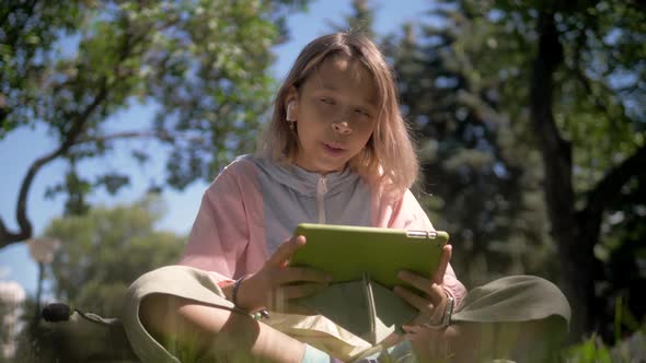 Cute Young Student Girl with Tablet Sitting in the Park, School Child Resting Outdoors