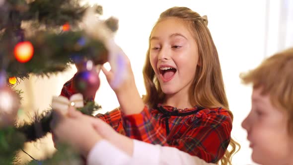 Smiling Beautiful Girl Decorating New Year Tree with Little Boy in Living Room at Home