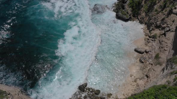 Aerial tilt up of waves breaking against cliffs, tropical coastline