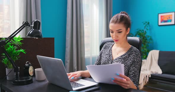 A Young Pretty Girl Works with Documents While Sitting at a Desk in a Cozy