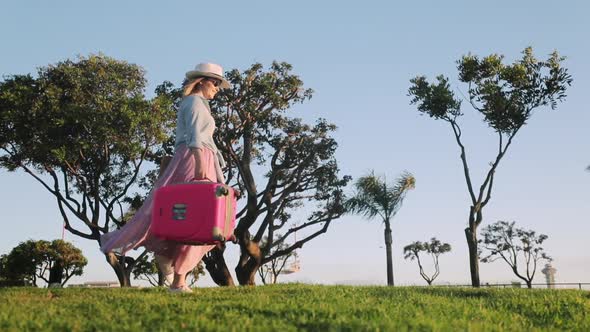 Cheerful Woman Excited About Her Travel, Jumping with Pink Travel Bag at Sunset