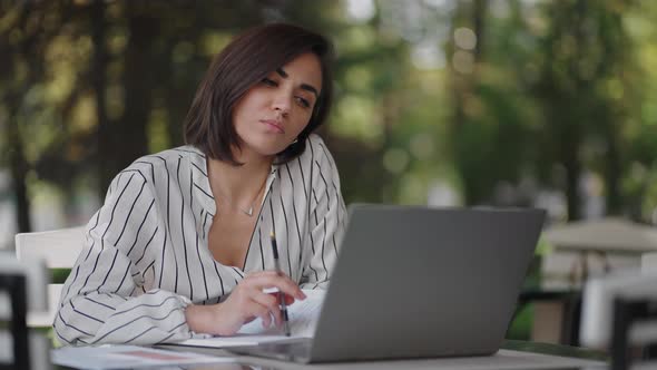 Pensive Woman Brunette Arabic Hispanic Ethnic Group Sits at a Table in a Summer Cafe with a Laptop