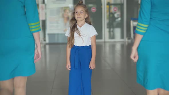 Pretty Caucasian Little Girl Admiring Stewardesses Entering Airport and Looking at Camera. Portrait