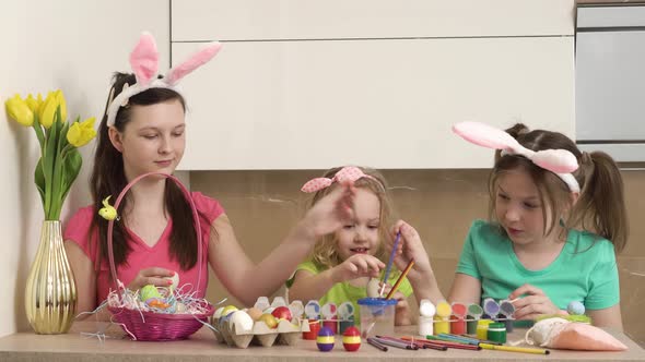 Three Beautiful Girls with Bunny Ears Paint Easter Eggs with Paint
