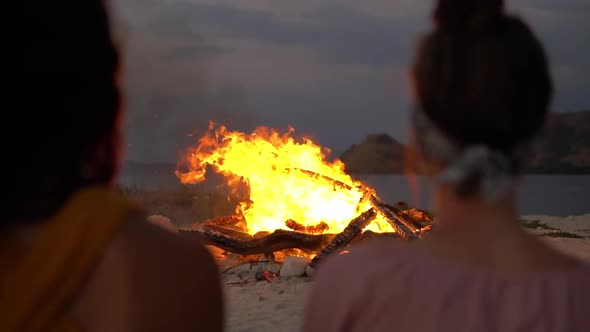 Close Up of a Fire on the Beach the Camera Pulls Back Showing Two Girlfriends Sitting Next to It and