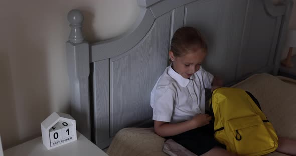 Cute Caucasian Primary School Girl Wearing Uniform and Packing Backpack at Home on Bed Kid Preparing