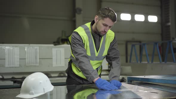 Portrait of Young Caucasian Man Measuring Steel Metal Sheet. Confident Professional in Vest and