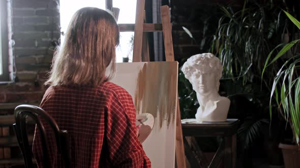 A Young Woman Artist in a Workshop Applying Base Colors on a Canvas with a Small Brush