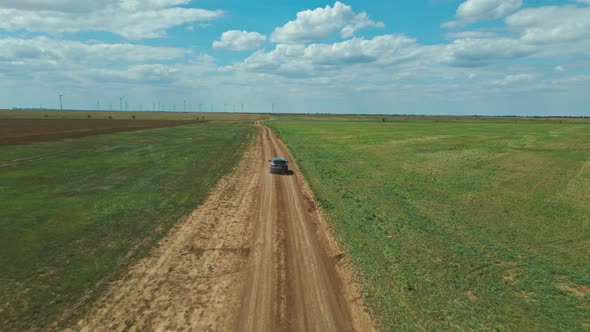 Aerial View From Drone Camera on Car Moving By Rustic Road Through Green Fields