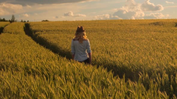 young caucasian bohemian female wearing hat in a  barley field during sunset