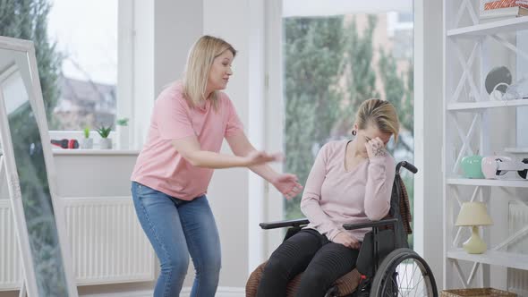 Joyful Young Caucasian Woman Cheering Up Handicapped Friend in Wheelchair