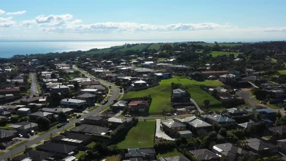 AERIAL Coastal Village Rising Over Sunny Bay Water And Green Hills