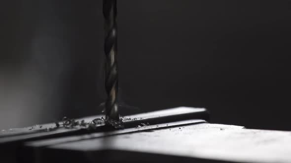 Detail steel bars being drilled by a drill press to create a structure in a machine shop.