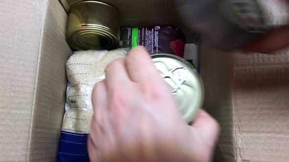 A Man Collects a Box of Humanitarian Aid for the Needy Rice Cereals Canned Goods in Tins