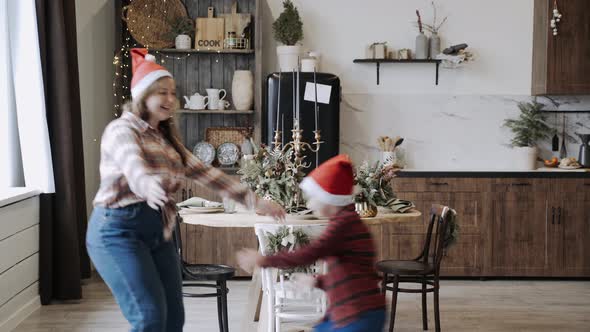 Caucasian Plump Mom and Son in Santa Hat Having Fun Near Festive Table and Hug