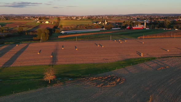 Amazing aerial over farmland and  bronze coloured pasture dotted with bales of hay  during sunset