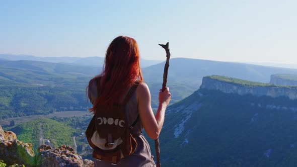 Girl with Backpack Staff Walks in Mountains