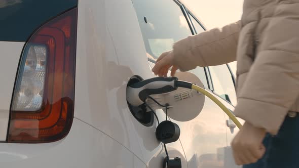 Woman Coming to the Electric Vehicle and Unplugging Power Supply Cable to Charge in the Street at