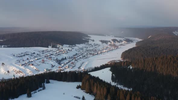 Aerial View of a Village with Wooden Houses on the Bank of a Frozen River in Winter