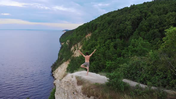 Young Shirtless Man Meditating on a Cliff Around the Forest in Early Morning