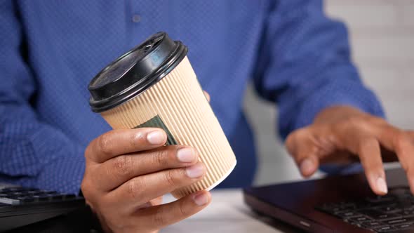 Hand Holding Paper Coffee Cup and Working on Laptop