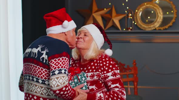 Senior Family Couple Grandmother Presenting Christmas Gift Box to Amazed Grandfather at Home Room