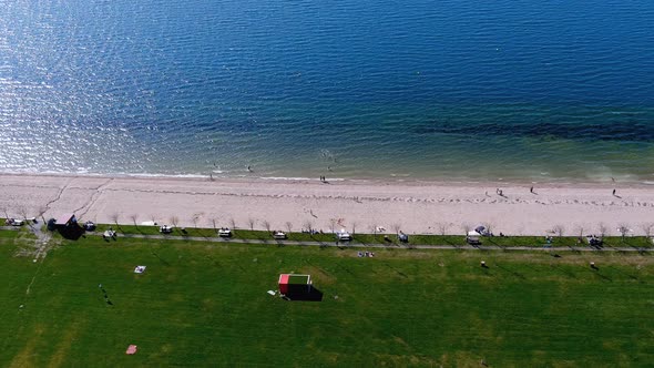 Lake beach with people sunbathing and bathing, garden and walking area. Overhead drone shot travelin