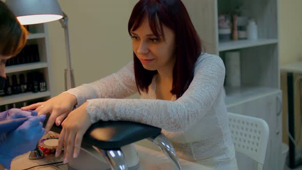 Young Woman Sits During Nail Care Procedure in Salon