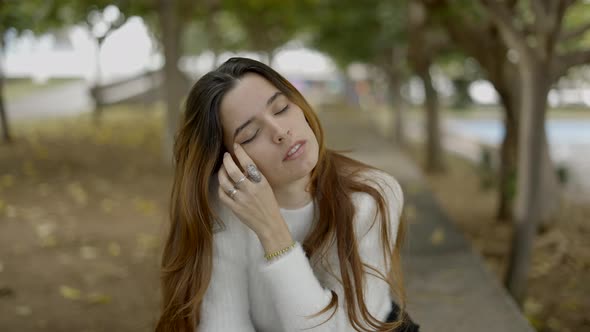 Close View of Young Brownhaired Woman in Park Touching Her Face