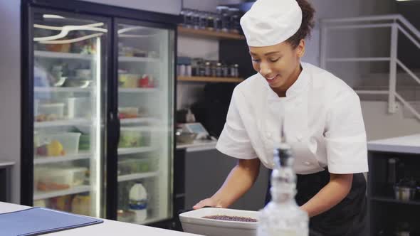 African American female chef wearing chefs whites in a restaurant kitchen,taking food out of an oven