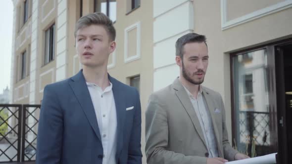Portrait of Two Cute Confident Men in Formal Wear Walking on Terrace Discussing New Project