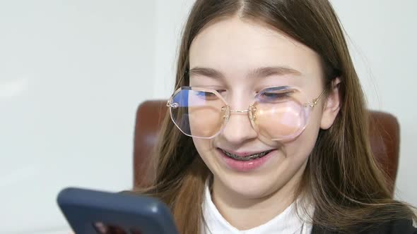 Cheerful Teen Girl in Formalwear Talking on Cell Phone Sitting at Computer on White Background