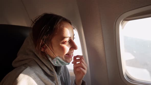 Closeup Shot of Happy Female Passenger in Protective Medical Face Mask Looking in Airplane Window