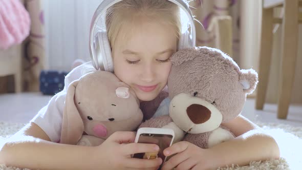 A School Girl Plays the Phone Lying on the Floor in Her Room, Along with Her Her Favorite Toys.