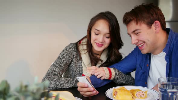 Couple using mobile phone while having breakfast