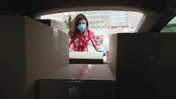 View From Car Trunk: Couriers, Man and Woman in Protective Masks, Gloves, Are Unloading Parcels