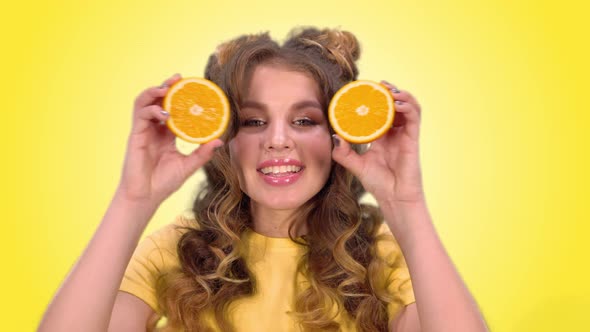 Beautiful Young Girl with Laying Posing with Oranges and Smiling Looking Into the Camera on a Yellow