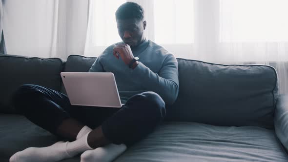 African American Black Man Using Laptop While Sitting on the Couch Crosslegged