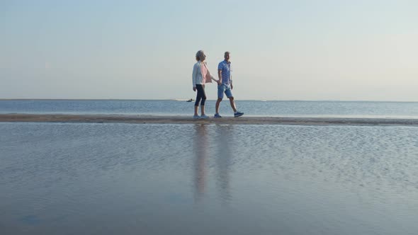 Happy Mature Couple in Love Walking and Holding Hands at Sea Shore