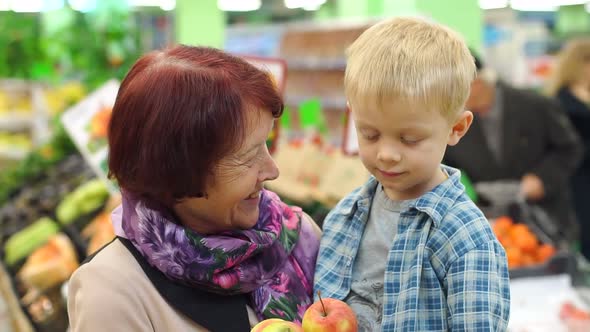 Grandmother with Her Little Grandson Buy Fresh Apples in a Large Supermarket.