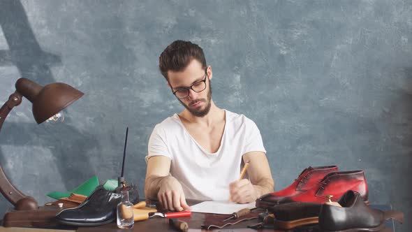 Footwear Designer Sitting at the Table and Drawing Model