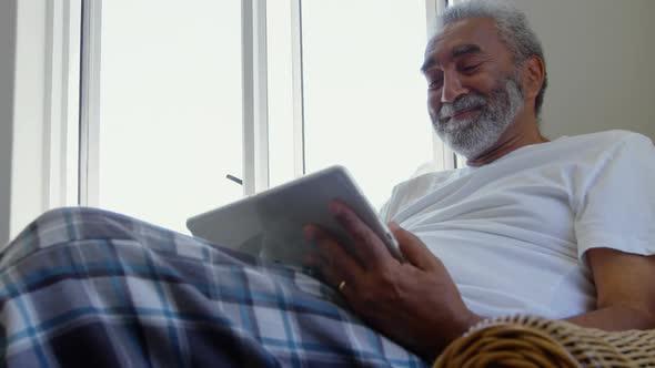 Front view of senior black man sitting on the couch and using digital tablet in comfortable home 4k