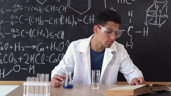 an Arab Man Sits in the Audience at a Table Against the Background of a Blackboard with Chemical