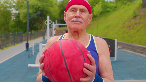 Healthy Senior Sportsman Guy Grandfather Practicing with Ball in Sport Playground Basketball Court