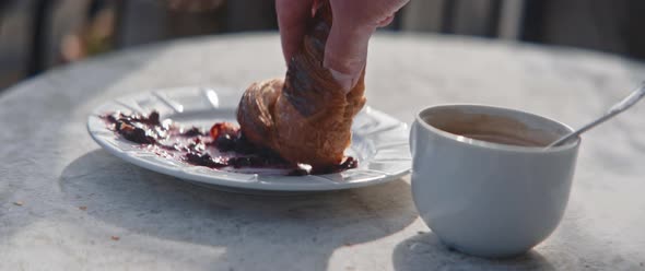 Closeup of hands of a man dipping croissant into jam