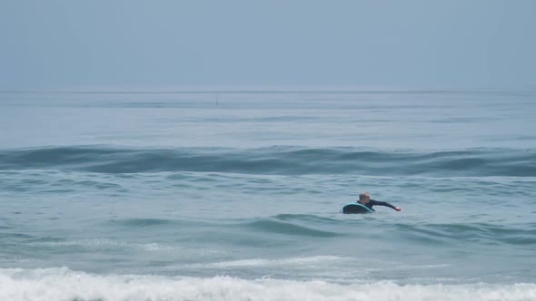 A Surfer on the Surf Board Floating in the Blue Sea While Waiting for Surf Waves
