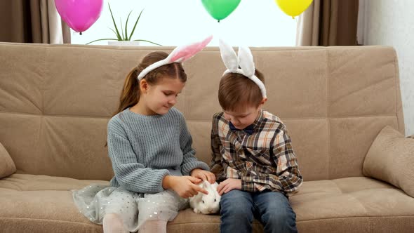 A Boy in Bunny Ears and a Girl are Stroking a White Fluffy Easter