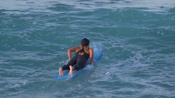 A young woman in a wetsuit paddling on her longboard surfboard.
