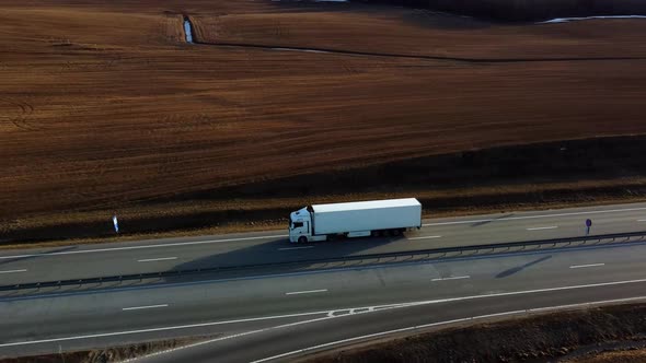 The white truck drives along the highway in the rays of the setting sun