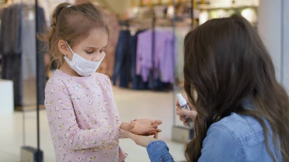 Mother sanitizing her daughter's hands with antibacterial hand spray. 